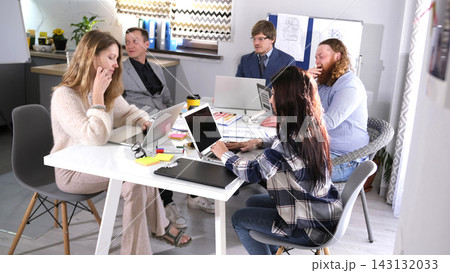 A small group of people are sitting at a table and working on a project on laptops. The atmosphere is relaxed A small group of people are sitting at a table and working on a project on laptops. The atmosphere is relaxed 143132033