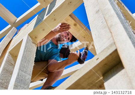 Roof truss connects wooden rafter legs while builder fastens timber joint using battery powered screwdriver. Roof truss connects wooden rafter legs while builder fastens timber joint using battery powered screwdriver. 143132718