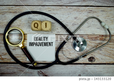 Quality Improvement (QI) text with stethoscope and magnifying glass on wooden background 143133120