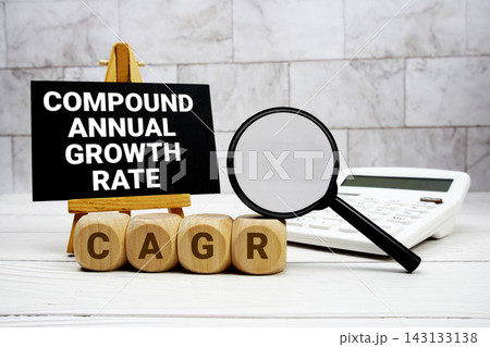 CAGR Compound Annual Growth Rate text with calculator magnifying glass and on wooden background 143133138