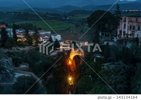 Illuminated bridge deep in the Tajo gorge at blue hour with birds flying over Ronda Illuminated bridge deep in the Tajo gorge at blue hour with birds flying over Ronda 143134164