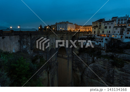 Stone arches of Puente Nuevo and cliffside houses above the gorge at blue hour in Ronda Stone arches of Puente Nuevo and cliffside houses above the gorge at blue hour in Ronda 143134168