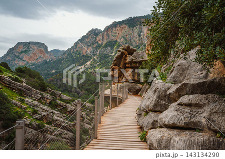 Wooden boardwalk winding past a boulder outcrop toward forested mountains at Caminito del Rey Wooden boardwalk winding past a boulder outcrop toward forested mountains at Caminito del Rey 143134290