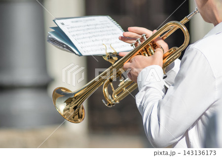 Musician Playing Trumpet Outdoors with Sheet Music in Hand 143136173