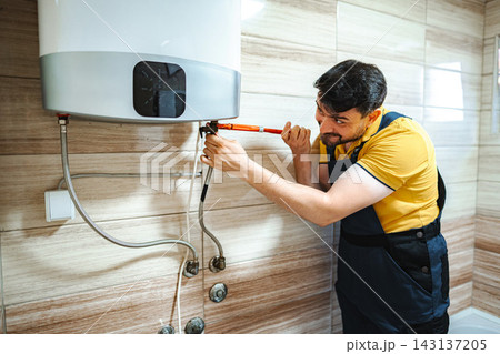 Plumber repairing water heater with a wrench in bathroom Plumber repairing water heater with a wrench in bathroom 143137205