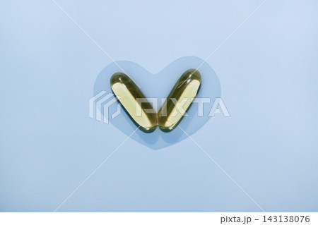 Two fish oil softgels creating heart shape on pastel blue background 143138076