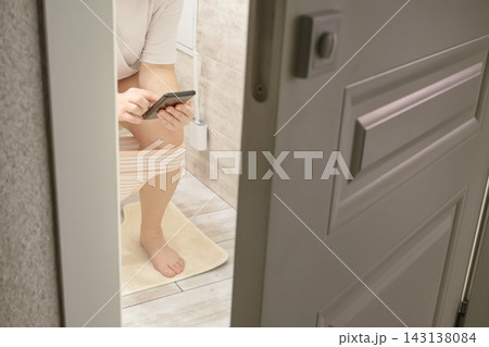 Person sitting on toilet using smartphone, seen through an open door Person sitting on toilet using smartphone, seen through an open door 143138084