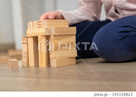 Young child hand carefully stacking natural wooden blocks, developing creativity, imagination, and motor skills while playing on a warm wooden floor indoors 143139823
