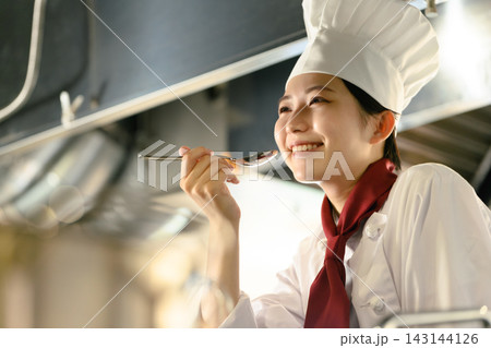 スプーンで味見をする笑顔の女性シェフ スプーンで味見をする笑顔の女性シェフ 143144126