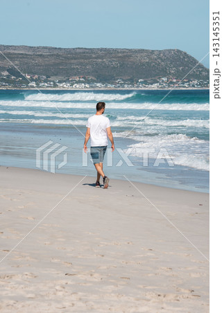 Man walking along a sandy beach near Cape Town with ocean waves 143145351