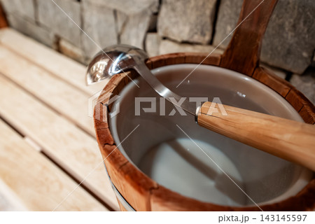 Wooden sauna bucket and metal ladle on benches by rough cut stone wall Wooden sauna bucket and metal ladle on benches by rough cut stone wall 143145597