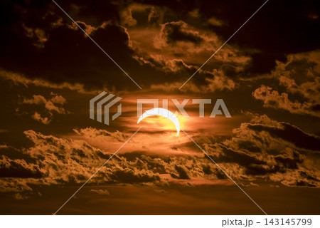Partial solar eclipse with glowing sun and dark clouds at sunset time Partial solar eclipse with glowing sun and dark clouds at sunset time 143145799