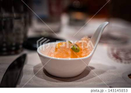 A white porcelain tasting spoon holds granita with an orange segment and green chili on a linen table in San Domenico, with warm light and shallow depth of field. A white porcelain tasting spoon holds granita with an orange segment and green chili on a linen table in San Domenico, with warm light and shallow depth of field. 143145853