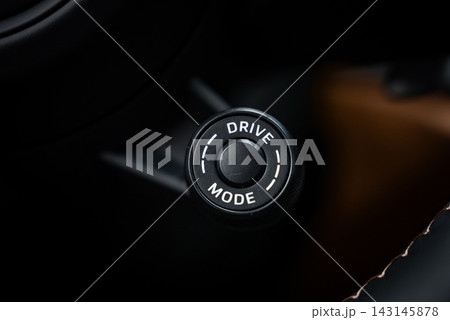 A close up shows the knurled Drive Mode rotary selector on a Porsche GT3 Touring, inside a workshop, with low key lighting, shallow depth of field, and brown upholstery. 143145878