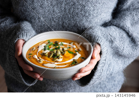 Bowl of pumpkin soup in woman hands 143145946