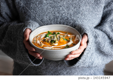 Bowl of pumpkin soup in woman hands 143145947