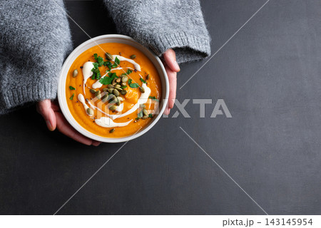 Female hands in knitted sweater holding bowl with pumpkin soup 143145954