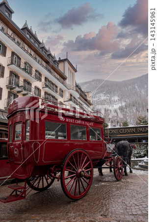 A red Mont Cervin Palace horse carriage waits by the historic hotel in Zermatt, Switzerland, with snow on alpine slopes and chalet balconies under soft overcast light. A red Mont Cervin Palace horse carriage waits by the historic hotel in Zermatt, Switzerland, with snow on alpine slopes and chalet balconies under soft overcast light. 143145961