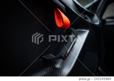 Close up shows Lamborghini Huracan door panel with carbon fiber, an orange fabric loop, and a slim Alcantara handle under soft natural light, suggesting track focus. Close up shows Lamborghini Huracan door panel with carbon fiber, an orange fabric loop, and a slim Alcantara handle under soft natural light, suggesting track focus. 143145964