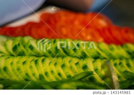 Neat rows of thin cucumber and tomato slices fill the frame in Oberlech, Austria. Soft indoor lighting and shallow depth of field suggest a kitchen prep station. 143145981