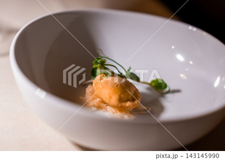 A golden fried dumpling rests on pickled vegetables and microgreens in a deep white bowl, warm focused lighting and shallow depth of field suggest fine dining in the Dolomites. 143145990