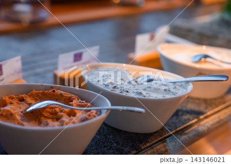 Three white bowls of gourmet spreads sit on a buffet in Oberlech, Austria, each with a metal spoon and tent card, under warm light with shallow depth and refined mood. Three white bowls of gourmet spreads sit on a buffet in Oberlech, Austria, each with a metal spoon and tent card, under warm light with shallow depth and refined mood. 143146021