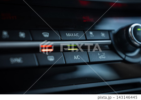 Close view of BMW X5 climate controls shows MAX AC and AC buttons lit, red and green bars, push buttons for defrost and recirculation, and a metallic rotary knob in low light. 143146445