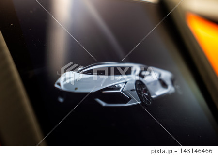 A touchscreen in a workshop displays a Lamborghini Revuelto render with Y light graphics and sharp lines. Glossy screen reflects soft light, hinting at orange bodywork nearby. 143146466