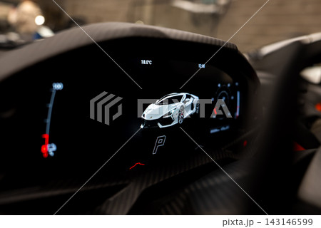 Digital instrument cluster of a Lamborghini Revuelto shows car render, gear P, 18.0 C, and tachometer gauge in a workshop with carbon fiber trim and dim light. Digital instrument cluster of a Lamborghini Revuelto shows car render, gear P, 18.0 C, and tachometer gauge in a workshop with carbon fiber trim and dim light. 143146599