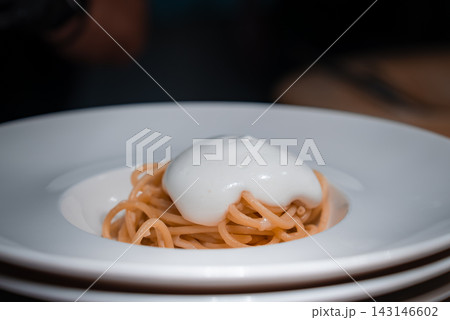 Close up spaghetti with glossy white foam in a deep white bowl, indoors in Oberlech, Austria. Soft moody lighting isolates the dish, suggesting fine dining style. 143146602