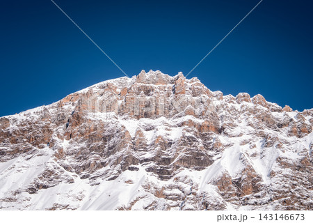 Stratified rock and jagged pinnacles rise under a deep blue sky near San Domenico, Italian Alps, in bright winter daylight, with minimal foreground and crisp detail. 143146673