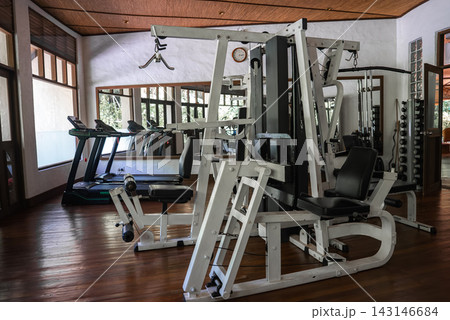 Daytime resort gym in Maldives shows multi station machine, treadmills, and free weights with mirrors, wood floors, high ceilings, and windows to tropical plants. Daytime resort gym in Maldives shows multi station machine, treadmills, and free weights with mirrors, wood floors, high ceilings, and windows to tropical plants. 143146684