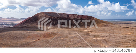 Rust red cone with horseshoe crater rim rises from lava plain, Atlantic gleams beyond. Small settlements sit at left, tiny hikers trace footpaths in daylight tones. 143146797