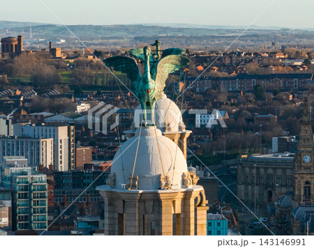 Aerial close up shows Liver Bird atop Royal Liver Building in Liverpool at sunrise. Verdigris copper, cables, ornate stonework, rooftops, clock towers, housing, and glass blocks. Aerial close up shows Liver Bird atop Royal Liver Building in Liverpool at sunrise. Verdigris copper, cables, ornate stonework, rooftops, clock towers, housing, and glass blocks. 143146991
