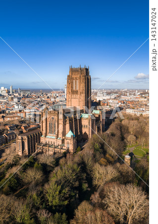 Aerial sunrise view shows Liverpool Cathedral in Liverpool, UK. Crisp light highlights the central tower, flying buttresses, and turrets, with docks and the Mersey beyond. 143147024