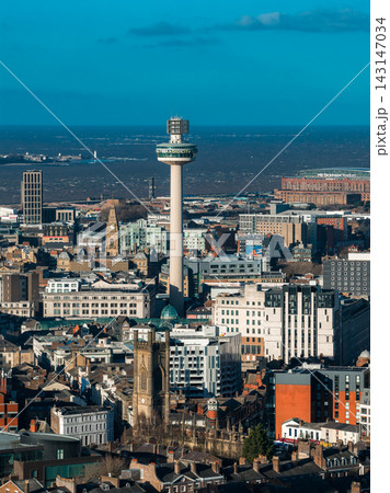 Aerial view of central Liverpool, UK, shows St John's Beacon, St Luke's Church tower, the River Mersey, and a waterfront stadium under clear daylight skies. 143147034