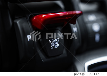Close up center console shows red flip up START ENGINE STOP cover, P and M H selectors, and angular surfaces of a Lamborghini Urus Performante in low key light. 143147130