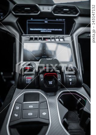 Close up interior view shows the START STOP red flip cover, Strada, Sport, Corsa, Neve toggles, carbon fiber trim, metallic accents, cup holders, and infotainment screen. 143147132