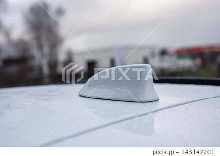 Close up shows the shark fin antenna on a Lexus RX 450h plus roof, beaded with raindrops, with blurred industrial buildings and bare trees on a cool rainy day. Close up shows the shark fin antenna on a Lexus RX 450h plus roof, beaded with raindrops, with blurred industrial buildings and bare trees on a cool rainy day. 143147201