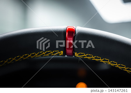 Close up macro shows a steering wheel red center marker at 12, thick black leather rim, bold yellow cross stitching, soft light, and an amber dash glow. Close up macro shows a steering wheel red center marker at 12, thick black leather rim, bold yellow cross stitching, soft light, and an amber dash glow. 143147261