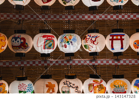 Rows of hand painted lanterns show torii, koi, masks, and calligraphy. Checkered trim and bamboo backdrop suggest a matsuri in Kyoto, Japan. Warm even light shows texture. 143147328
