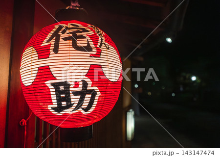 A red paper lantern with black and white kanji hangs at a wooden storefront in Kyoto at night, shot close up with shallow depth of field and soft bokeh lights. A red paper lantern with black and white kanji hangs at a wooden storefront in Kyoto at night, shot close up with shallow depth of field and soft bokeh lights. 143147474