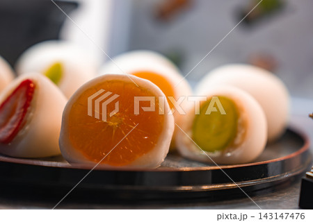 Close up shows strawberry, grape, and halved mandarin daifuku on a lacquered tray in Kyoto, Japan. Warm light and shallow depth reveal glossy fruit and soft mochi. 143147476