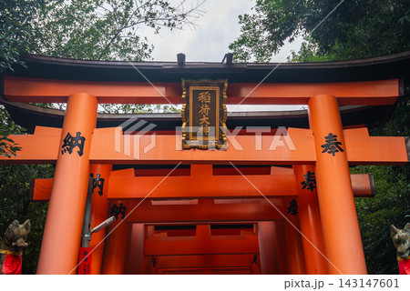 Vermilion torii gates rise in sequence at Fushimi Inari Taisha in Kyoto, Japan, a gilded plaque centered on the front gate under soft overcast daytime light 143147601
