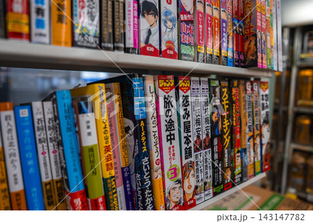 Rows of Japanese manga fill tidy shelves in an Osaka shop. Bold kanji titles and character art line colorful spines, eye level view, shallow depth, diagonal framing. Rows of Japanese manga fill tidy shelves in an Osaka shop. Bold kanji titles and character art line colorful spines, eye level view, shallow depth, diagonal framing. 143147782