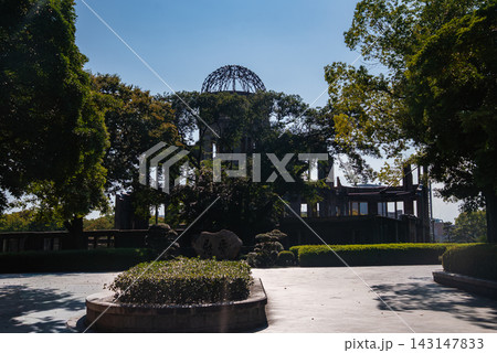 Hiroshima Peace Memorial in Hiroshima, Japan, shows the skeletal dome and ruined walls, framed by trees, with trimmed hedges and a circular planter in the plaza foreground. Hiroshima Peace Memorial in Hiroshima, Japan, shows the skeletal dome and ruined walls, framed by trees, with trimmed hedges and a circular planter in the plaza foreground. 143147833