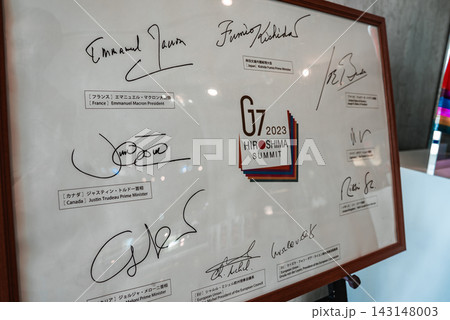 A framed G7 2023 Hiroshima Summit emblem sits with bold leader signatures and labeled nameplates in Hiroshima, Japan, presented in a museum style display. A framed G7 2023 Hiroshima Summit emblem sits with bold leader signatures and labeled nameplates in Hiroshima, Japan, presented in a museum style display. 143148003