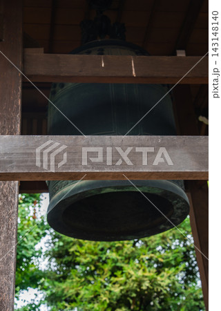 A large bronze bonsho hangs in a wooden belfry in Tokyo, close view shows patina and form, beams frame the bell, soft light suggests ritual use and quiet focus 143148140