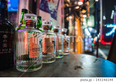 Empty Hibiki Japanese Harmony bottles on a small round table outside a bar, neon city lights blur behind, shallow depth of field and colorful bokeh in Tokyo. Empty Hibiki Japanese Harmony bottles on a small round table outside a bar, neon city lights blur behind, shallow depth of field and colorful bokeh in Tokyo. 143148144