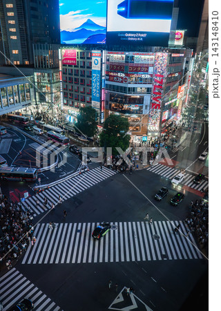 Shibuya Crossing in Tokyo at night shows white stripes, crowds, taxis, cars, neon signs, and a large digital screen, capturing the busy urban energy and flow. Shibuya Crossing in Tokyo at night shows white stripes, crowds, taxis, cars, neon signs, and a large digital screen, capturing the busy urban energy and flow. 143148410